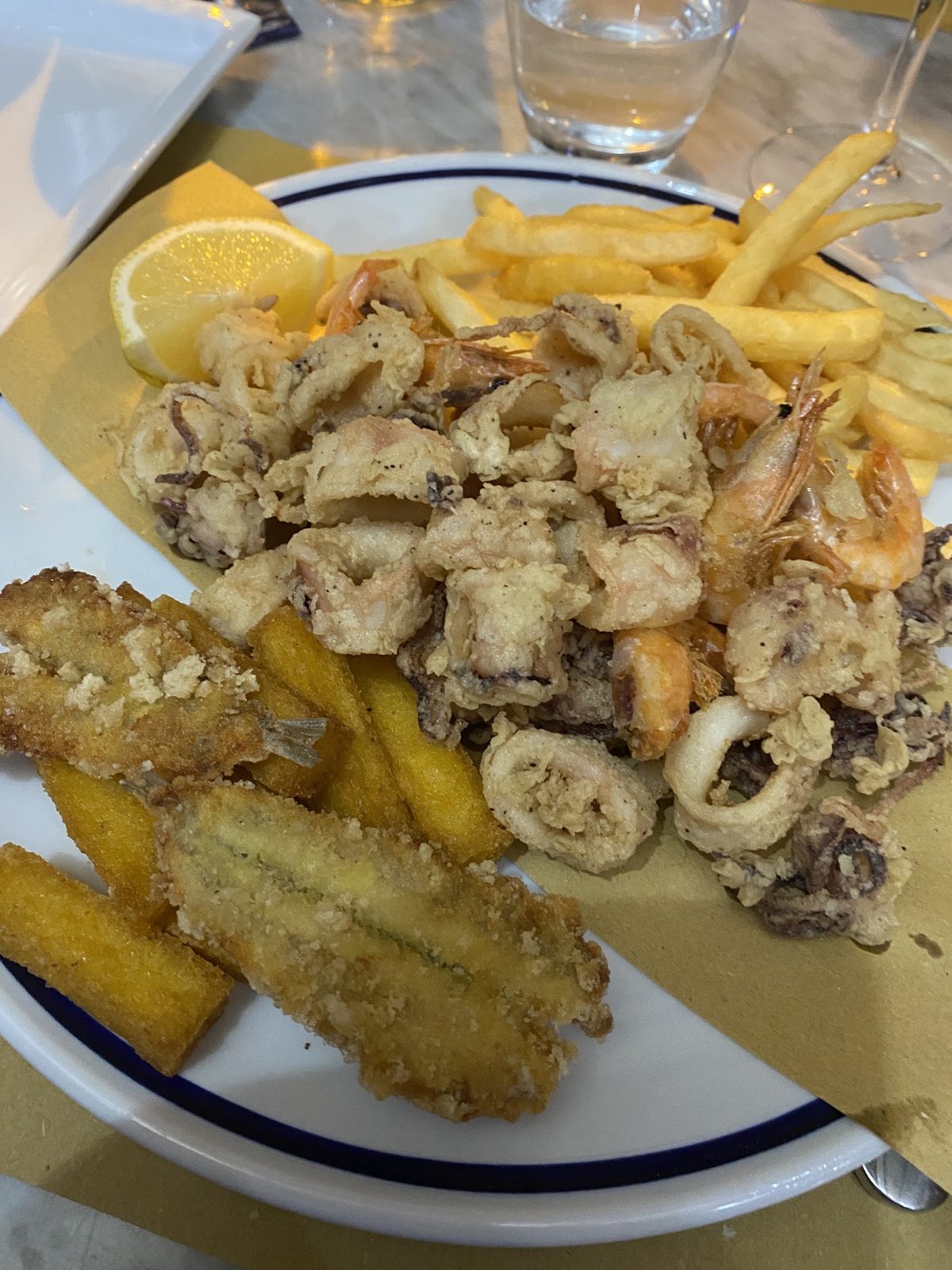 Fritto misto di mare con calamari, gamberi e verdure fritte, servito con spicchi di limone e patatine.