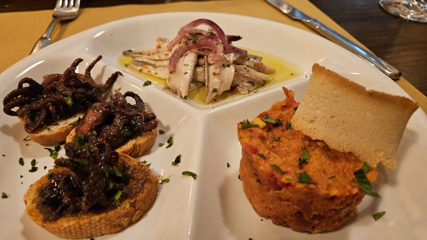 Tre crostini serviti su un piatto: polpo con olio e prezzemolo, un&rsquo;insalatina di mare e una crema rossa.