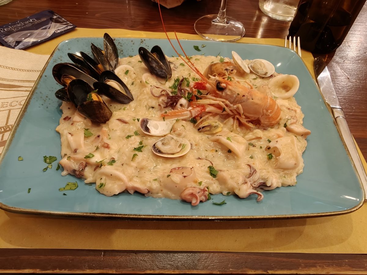 Risotto ai frutti di mare con cozze, vongole, calamari e un gambero, servito su un piatto azzurro.